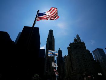 Low angle view of national flags at michigan avenue bridge by skyscrapers against sky
