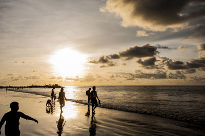 People walking at beach against sky during sunset