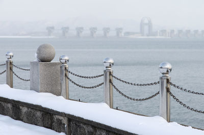 Railing by sea against sky during winter