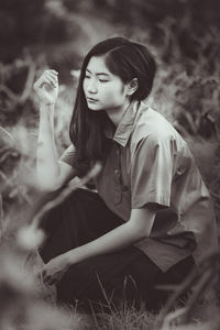 Young woman looking away while sitting on land