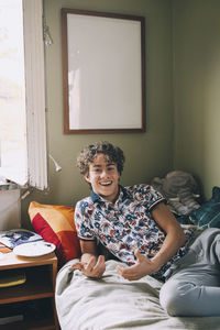 Portrait of cheerful teenage boy leaning on bed at home