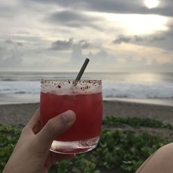 Midsection of person holding drink at beach against sky