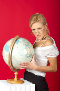 Portrait of businesswoman standing by globe against red background