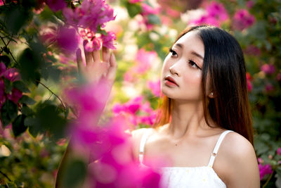 Portrait of beautiful woman standing by pink flowering plant