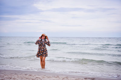 Smiling woman wearing dress standing at beach against sky