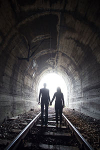 Rear view of silhouette people standing on railroad track