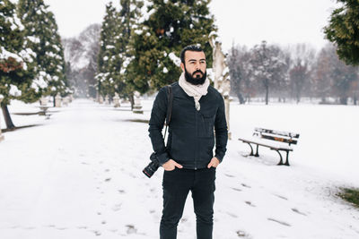 Handsome man with camera standing on snow covered footpath during winter
