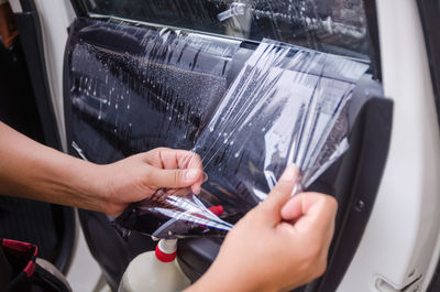 Cropped hands of woman removing plastic from car window