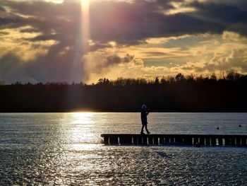 Silhouette man standing by lake against sky during sunset