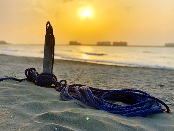 Close-up of rope on wooden post at beach against sky during sunset