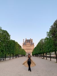 Rear view of woman walking on street against clear sky