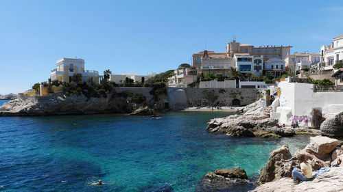 Buildings by sea against clear blue sky