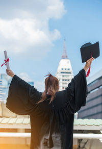 Woman in graduation gown standing against sky