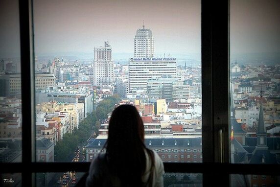 REAR VIEW OF MAN LOOKING THROUGH CITYSCAPE WINDOW