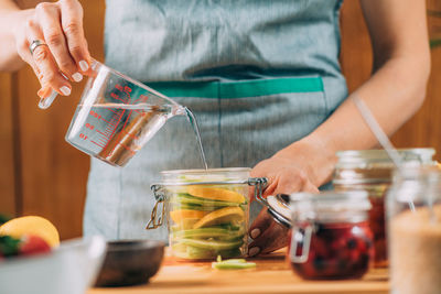 Midsection of woman holding glass jar on table