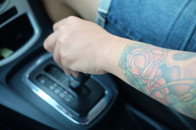 Midsection of tattooed man holding gearshift in car