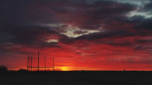 Silhouette electricity pylon on field against dramatic sky during sunset