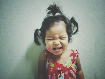 Portrait of cute baby girl crying while standing against wall