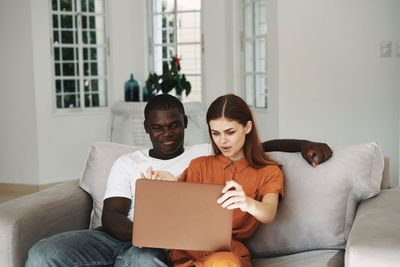 Couple using laptop while sitting on sofa at home