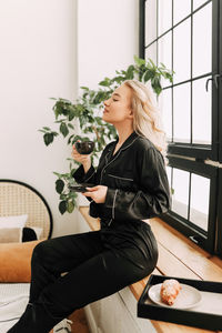 Woman sitting by potted plant at home