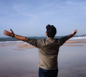 Rear view of man standing at beach against sky