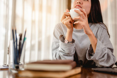 Midsection of woman sitting with cup at desk