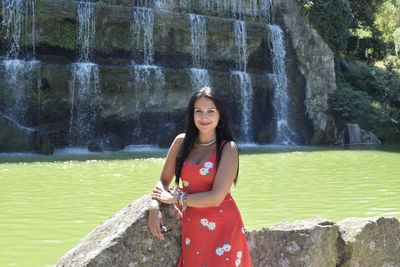 Portrait of beautiful woman wearing dress standing against fountain