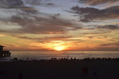 Silhouette people on beach against sky during sunset