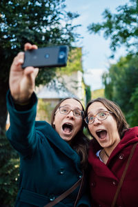 Twins making face while taking selfie with smart phone