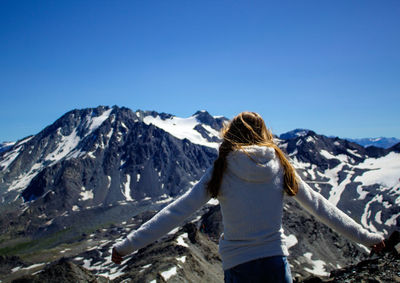 Rear view of woman with arms outstretched standing against snowcapped mountain