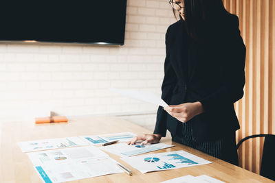 Midsection of woman analyzing graphs on table against wall