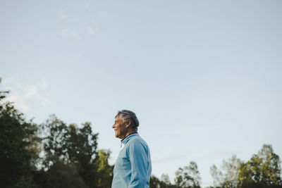 Side view of man looking at trees against sky