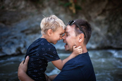 Like father like son. middle aged father embracing cute little son on the bank of river, family