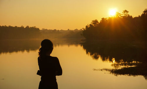 Silhouette woman standing by lake against sky during sunset