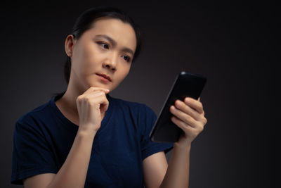Young woman using mobile phone against black background