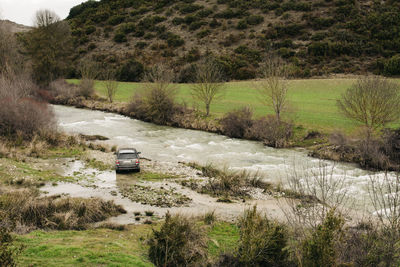 Modern suv parked on shore of rapid river flowing in hilly terrain covered with plants