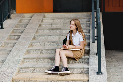 Full length of woman using mobile phone while sitting on staircase