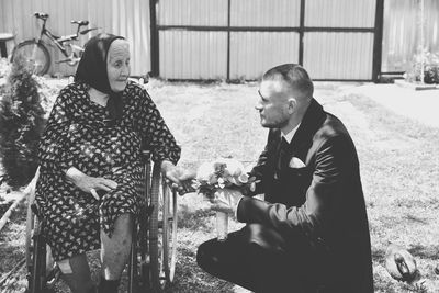 Man crouching by mother sitting on wheelchair in yard