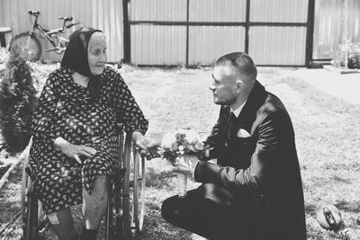 Man crouching by mother sitting on wheelchair in yard