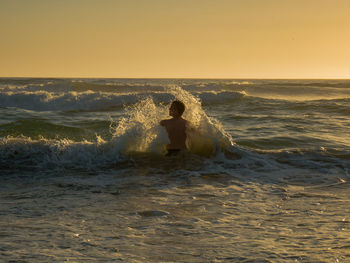 Boy on beach against clear sky during sunset