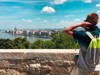 Rear view of man photographing cityscape against sky