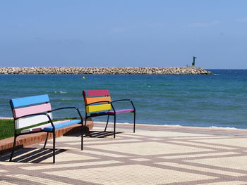 Chair on swimming pool by sea against clear sky