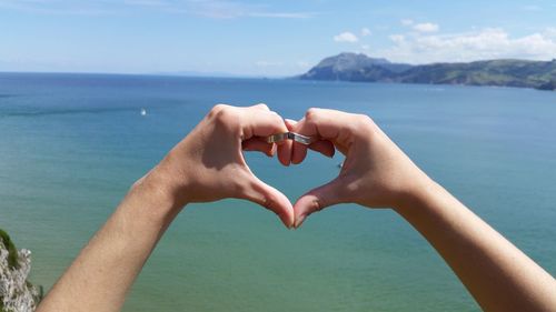 Close-up of hand holding heart shape against sea