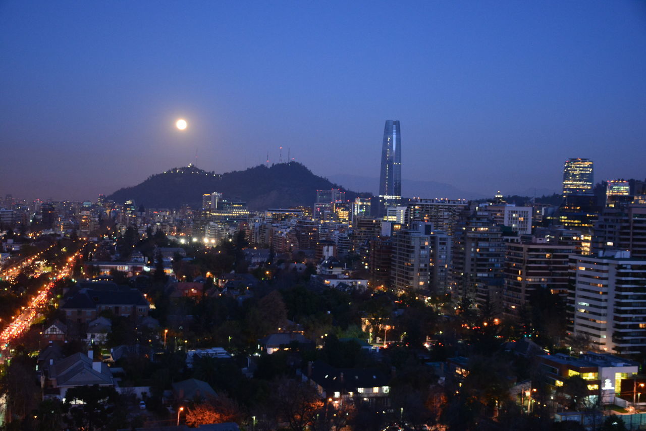 HIGH ANGLE VIEW OF ILLUMINATED CITYSCAPE AGAINST BLUE SKY