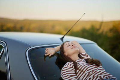 Portrait of young woman sitting on car