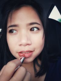 Close-up of young woman applying lipstick in car