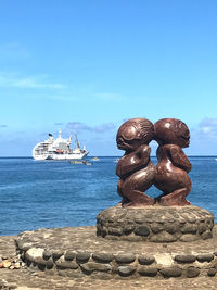 Stack of sculpture by sea against blue sky