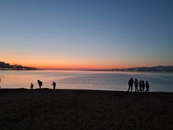 Silhouette people on beach against sky during sunset