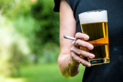 Midsection of woman having beer while smoking cigarette outdoors
