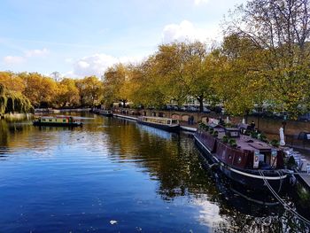 Boats moored on river by trees against sky